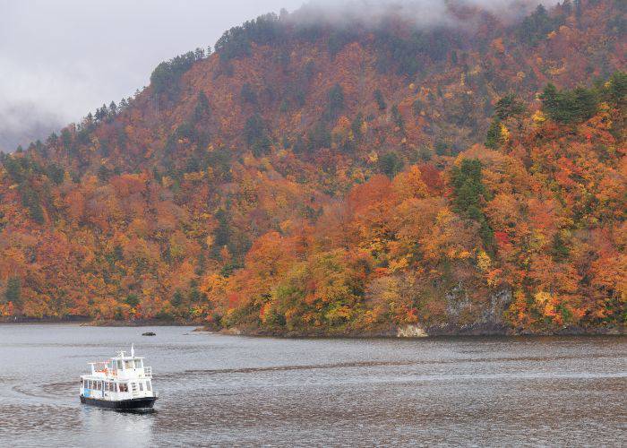 The Lake Okutadami pleasure cruise, floating across the surface of the lake as fall foliage decorates the background.